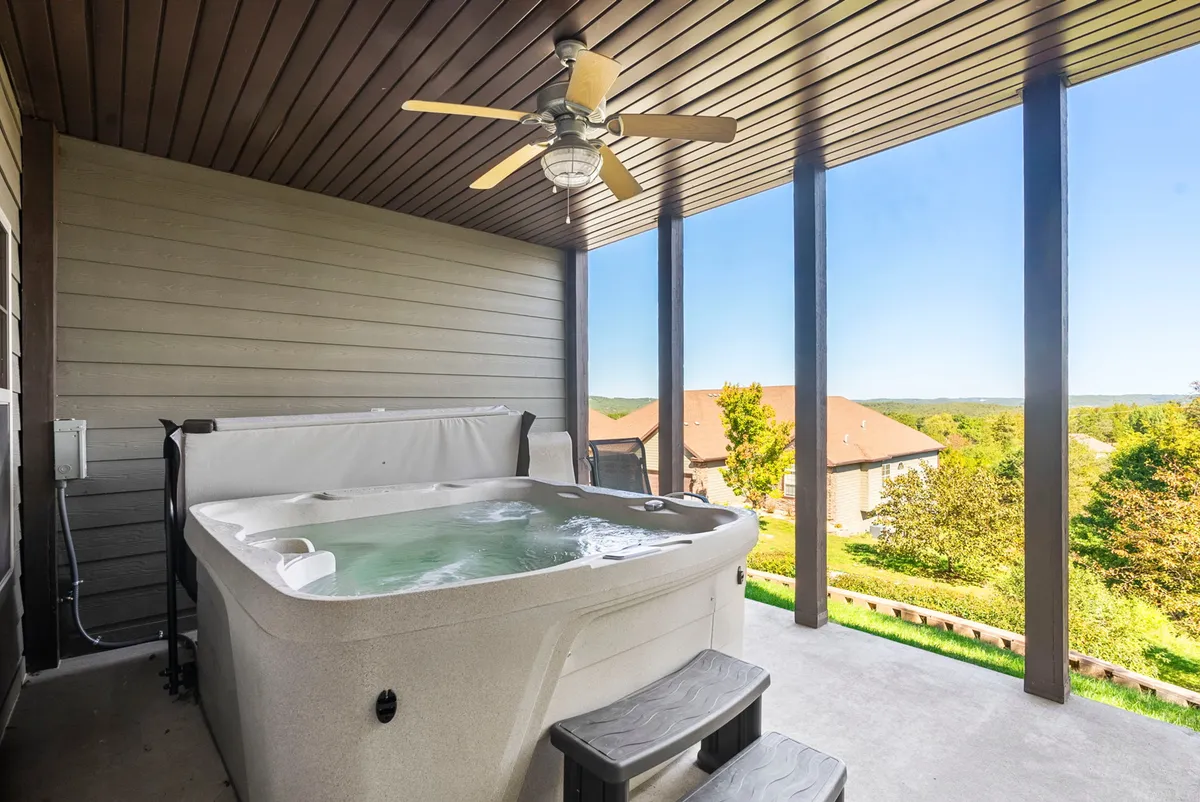 This image captures a tranquil outdoor hot tub set on a screened-in lower deck overlooking scenic views. The hot tub area is shaded and private, ideal for unwinding after an active day, and the view of the landscape beyond the deck enhances the sense of escape and relaxation.