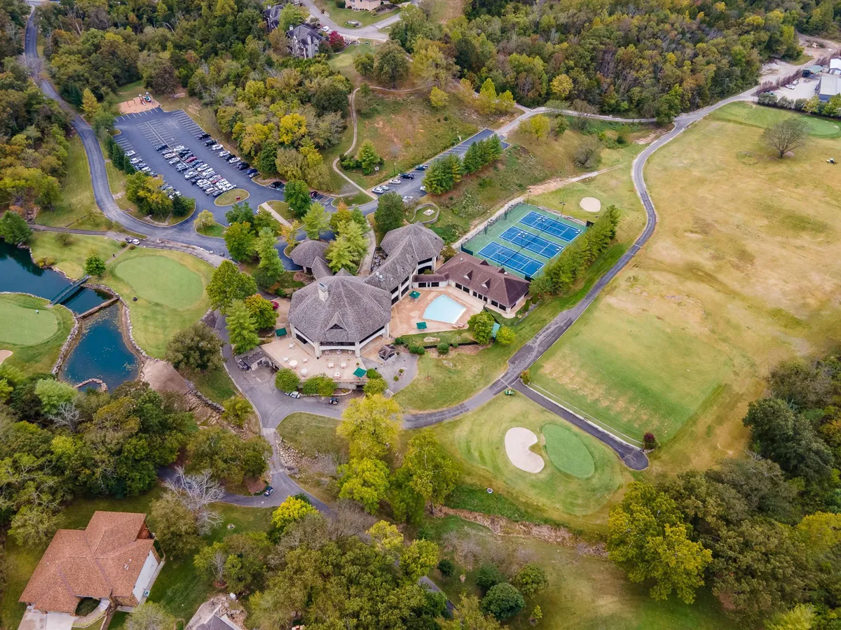 A wide exterior shot that features the main building, a swimming pool, tennis courts, a golf course, and a pond, all surrounded by lush landscaping. This comprehensive view encapsulates the variety of resort amenities and the expansive, nature-filled grounds.