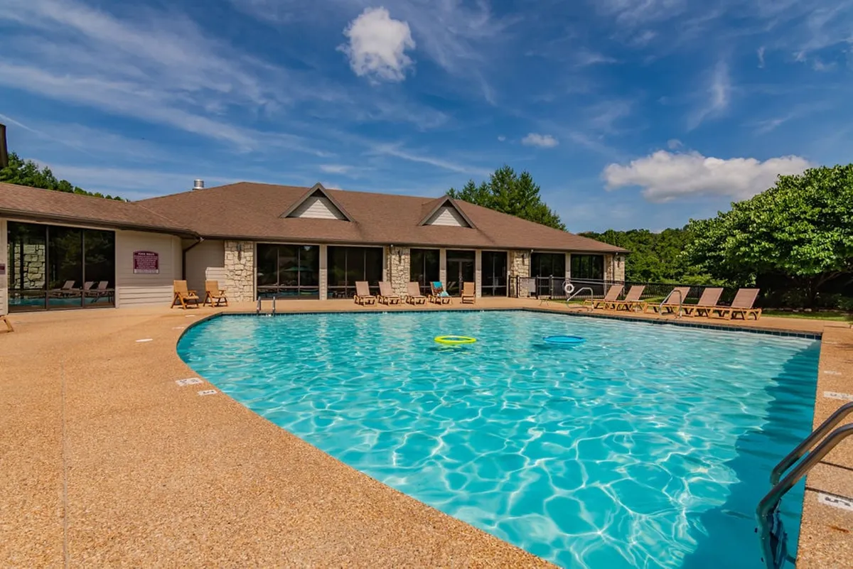 An inviting resort pool area with plenty of lounge chairs, surrounded by trees and the exterior of resort buildings. The space is ideal for sunbathing, swimming, or socializing with fellow guests, conveying a resort-like atmosphere and the outdoor amenities available.