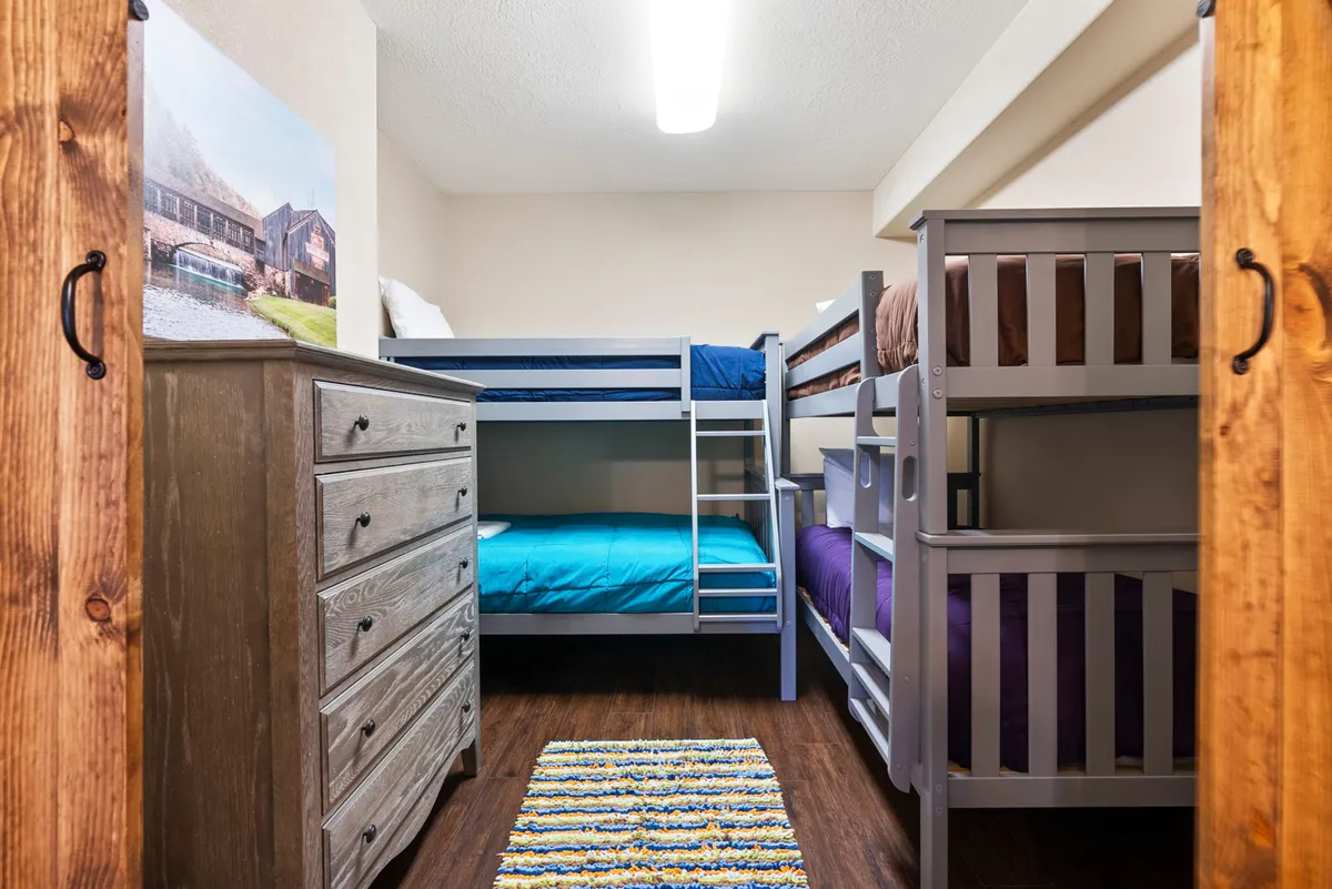 A playful bunk room with multiple bunk beds, a dresser, and a colorful rug. The space exudes a relaxed and cheerful vibe, perfect for kids and teens to unwind, play games, or share stories before bedtime.