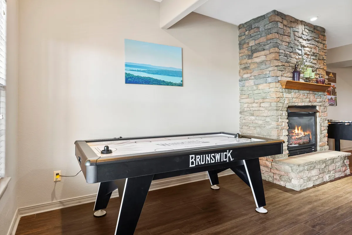 This image shows a lively game area featuring an air hockey table in a cozy, inviting setting. The stone fireplace adds warmth to the space, while a framed landscape painting and soft lighting create a welcoming mood. The area is clearly designed for both friendly competition and relaxation, perfect for group gatherings or family fun.