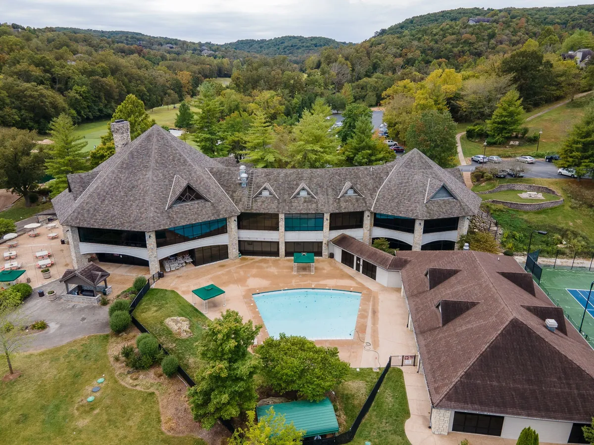A stunning exterior view of a resort pool surrounded by landscaped gardens, modern architecture, and a tennis court. The inviting pool glistens in the sunlight, suggesting opportunities for swimming, sunbathing, and social gatherings in a vibrant resort setting.