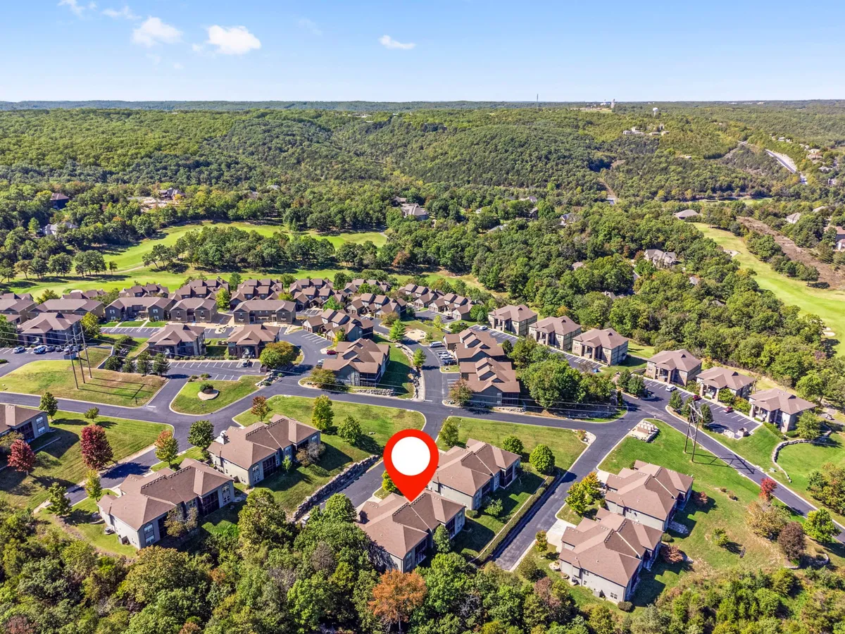 An expansive exterior shot capturing the neighborhood layout with residential buildings nestled among lush greenery. Visible in the scene is a portion of the golf course, framed by tree-lined hills, conveying a sense of community integrated with the natural landscape and recreational amenities.