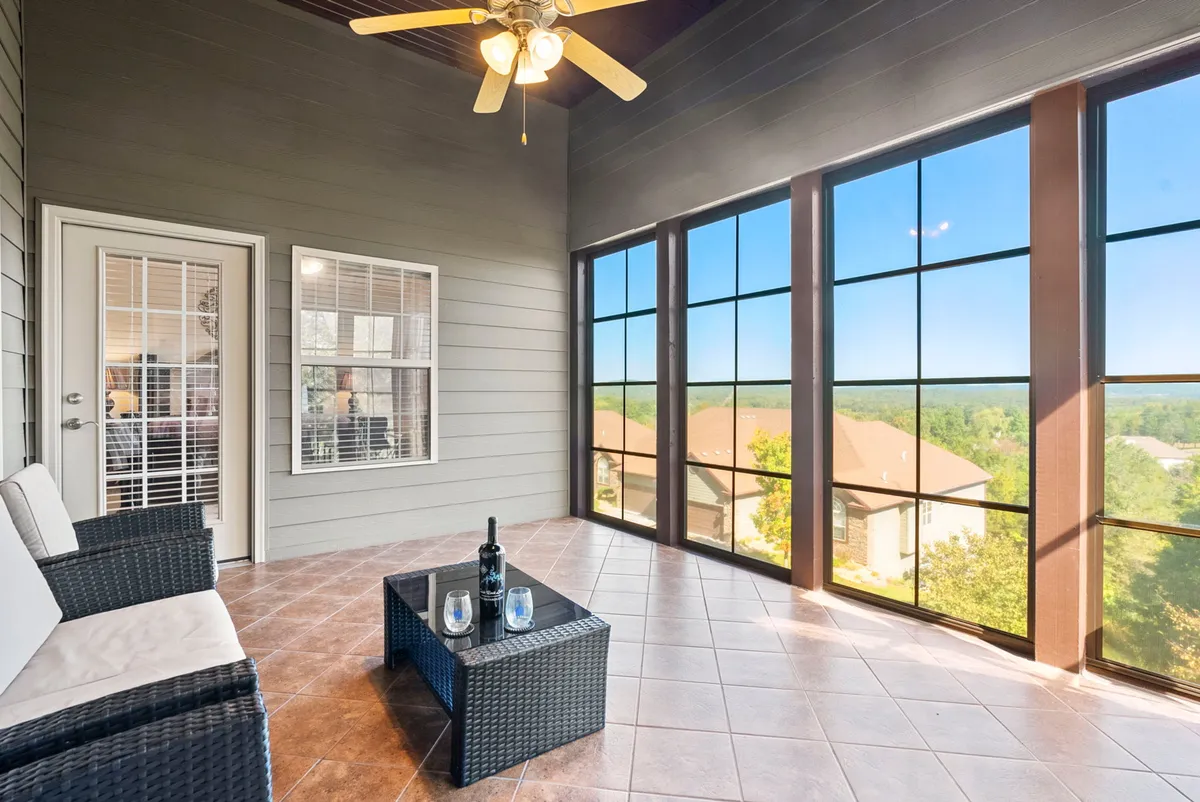 This image showcases a stylish seating arrangement beside large glass windows, with a serene woodland backdrop visible through the windows. The space is designed for relaxation and enjoying the natural views, enhanced by a decorative ceiling fan and wine bottle set out for quiet moments.
