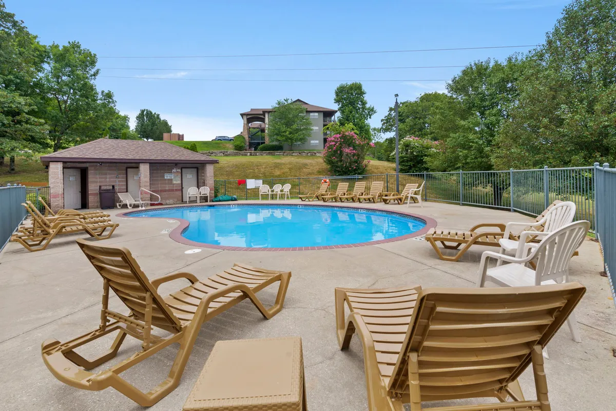 A serene outdoor pool scene with lounge chairs and a poolside cabana, surrounded by trees. The setting is perfect for sunbathing, swimming, or relaxing with friends and family in a tranquil environment.