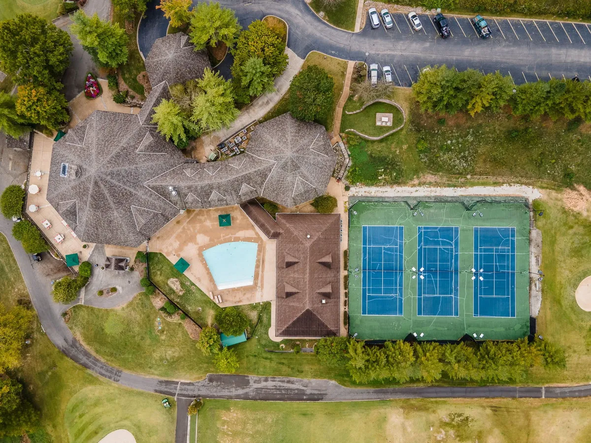A vibrant exterior view of StoneBridge Resort’s main amenities area, featuring the swimming pool, tennis courts, landscaped gardens, and the main building. The poolside setup and tennis courts highlight opportunities for recreation and gatherings in the heart of the resort community.